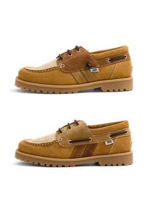 Paire de chaussures décontractées en suède beige et marron à lacets, semelles épaisses en caoutchouc, coutures visibles et petite étiquette en tissu "Caval" sur les côtés.