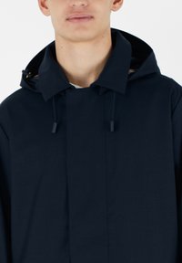 Giacca con cappuccio blu navy in un tessuto liscio, caratterizzata da un design semplice con colletto alto e cordini regolabili.