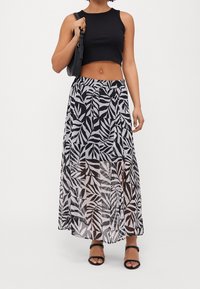 Black cropped top paired with a long, flowing black and white leaf-patterned skirt. Skirt features slits and a lightweight, sheer texture.