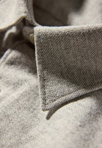 Grijs gestructureerde stof met een close-up van een kraag en knoop, die een geweven patroon en een zachte uitstraling toont.