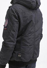 Giacca nera trapuntata con cappuccio, dotata di una patches con logo sulla spalla, polsini a coste e una finitura texturizzata.