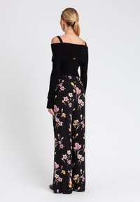 Top nero con spalle scoperte e maniche lunghe, abbinato a pantaloni a gamba larga con stampa floreale alta in vita, caratterizzati da fiori rosa e gialli su uno sfondo nero.
