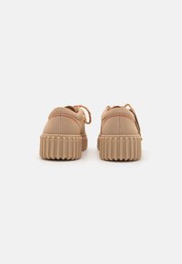 Chaussures en daim tan avec semelle en caoutchouc beige nervurée. Présentent des coutures et des lacets orange. Forme arrondie avec un design décontracté.