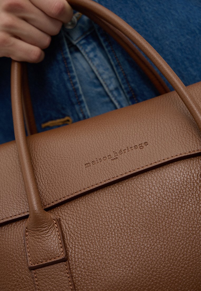 Braune Leder-Tote-Tasche mit strukturierten Oberflächen und zwei Griffen. Mit geprägtem Markennamen auf der Vorderseite. Weiches, strukturiertes Design.