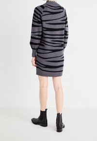 Grijze gebreide jurk met zwarte zebrastripes, geribde halslijn en ballonmouwen. Gestyled met zwarte enkellaarzen.