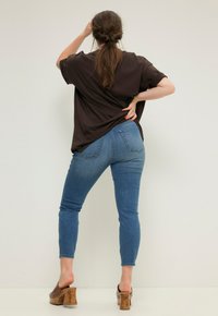 Camiseta marrón de gran tamaño, jeans ajustados azules, tacones de plataforma de madera. El conjunto presenta un ajuste relajado con una textura suave y costuras sutiles.