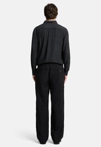 Schwarzes Langarmhemd mit Button-Down-Kragen und lockeren schwarzer Hose. Der Stoff wirkt strukturiert und weich, mit einem lässigen Design.