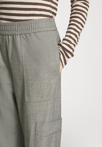 Gray herringbone cargo pants with side pockets and an elastic waistband, paired with a brown and white striped long-sleeve top.