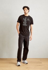 Camiseta de algodón negra con un gráfico de Mickey Mouse en diseño de tablero de ajedrez, combinada con pantalones cargo negros y zapatillas grises con detalles en blanco.