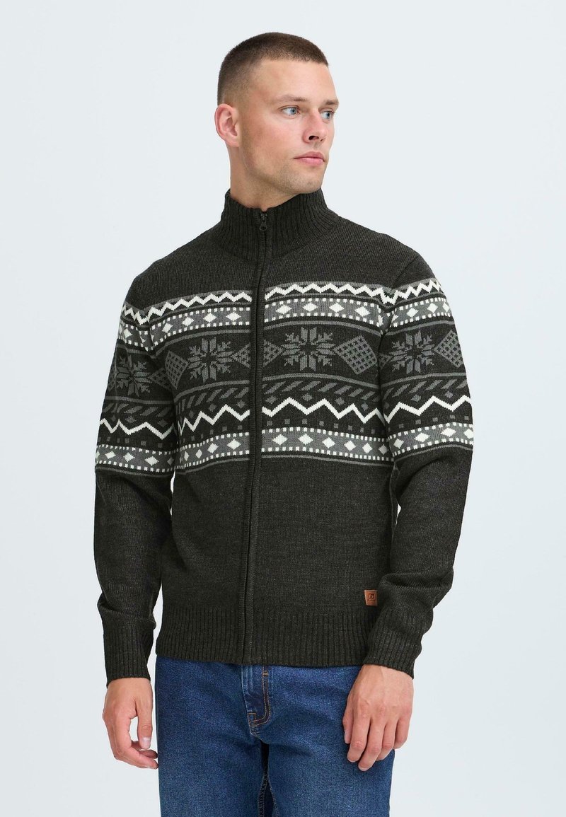 Mörkgrön stickad tröja med hög krage som har fair isle-mönster i vitt och grått över bröstet. Dragkedja framtill och ribbad mudd.