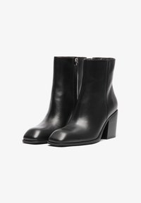 Botas de tobillo de cuero negro con un acabado suave, punta cuadrada y un tacón cuadrado de altura media. Con cremallera lateral para facilitar su uso.