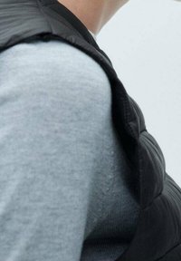 Czarna pikowana kamizelka na jasnoszarym swetrze, z wysokim kołnierzem i gładką, gładką fakturą tkaniny bez widocznych zapięć.