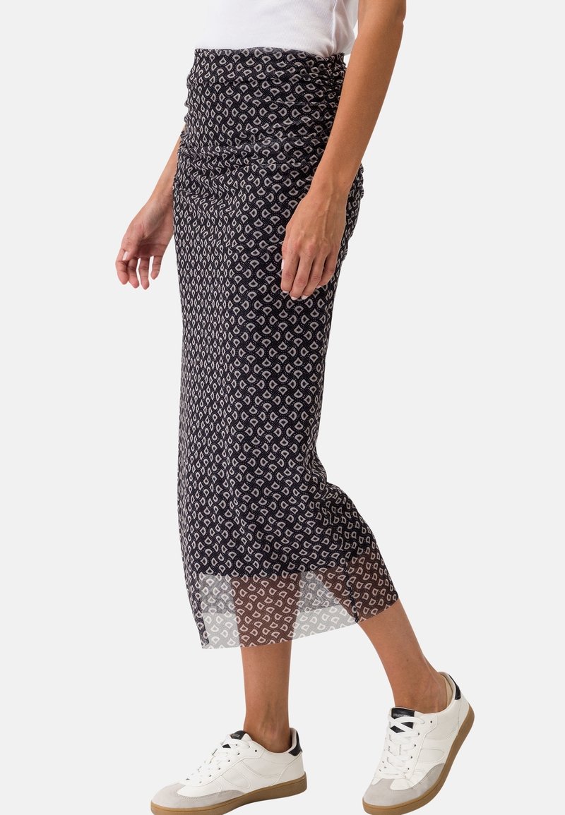 Jupe midi noire avec un motif texturé en losanges blancs, dotée d'une taille froncée et d'un ourlet semi-transparent, associée à des baskets blanches.