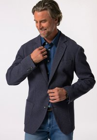 Granatowy żakiet o fakturowanej strukturze z dopasowanym krojem, z pojedynczą kieszenią na piersi i dwiema kieszeniami z przodu, noszony na koszuli dżinsowej.