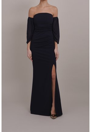 Granatowa sukienka z odkrytymi ramionami, wykonana z gładkiej tkaniny, z długimi przezroczystymi rękawami i wysokim rozcięciem po boku sięgającym uda. Sylwetka o długości do kolan, dopasowana.