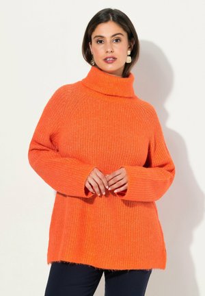 Pull en tricot orange avec un col montant, des manches larges, une texture côtelée et une coupe ample, associé à un pantalon sombre.