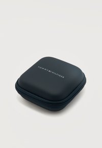 Συμπαγές μαύρο θήκη με φερμουάρ, με το λογότυπο Tommy Hilfiger και το έμβλημα της σημαίας στην κορυφή, σχεδιασμένη για την αποθήκευση μικρών προσωπικών αντικειμένων ή αξεσουάρ.