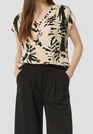 Kortærmet bluse i beige med sorte bladmønstre, udstyret med V-hals design. Sammenkobling af løse sorte bukser med elastisk talje.