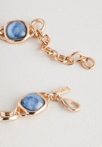 Gold-tone chain bracelet featuring a blue stone centerpiece and a lobster clasp, showcasing smooth, polished metal and a glossy finish.