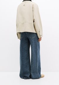 Beige cropped jasje met een rugstrook; wijd uitlopende blauwe jeans met een subtiel luipaardprintpatroon en een losse pasvorm. Zachte stofstructuur.