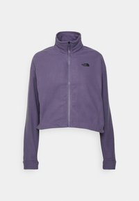 Przycięta purpurowa polarowa kurtka z wysokim kołnierzem, przednim zamkiem błyskawicznym i czarnym logo na lewej piersi. Miękka tekstura i długie rękawy.