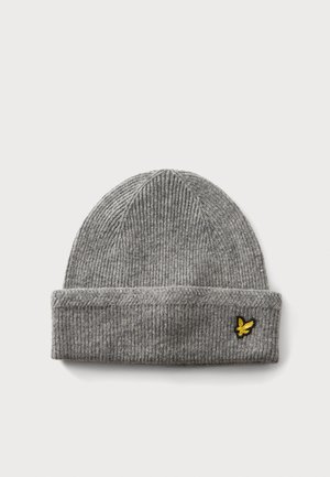 Bonnet gris en maille côtelée avec bord replié et petit emblème d'oiseau jaune sur le revers sur fond blanc.