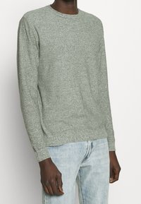 Jersey de punto gris con cuello redondo, puños acanalados y tejido texturizado, combinado con vaqueros azul claro.