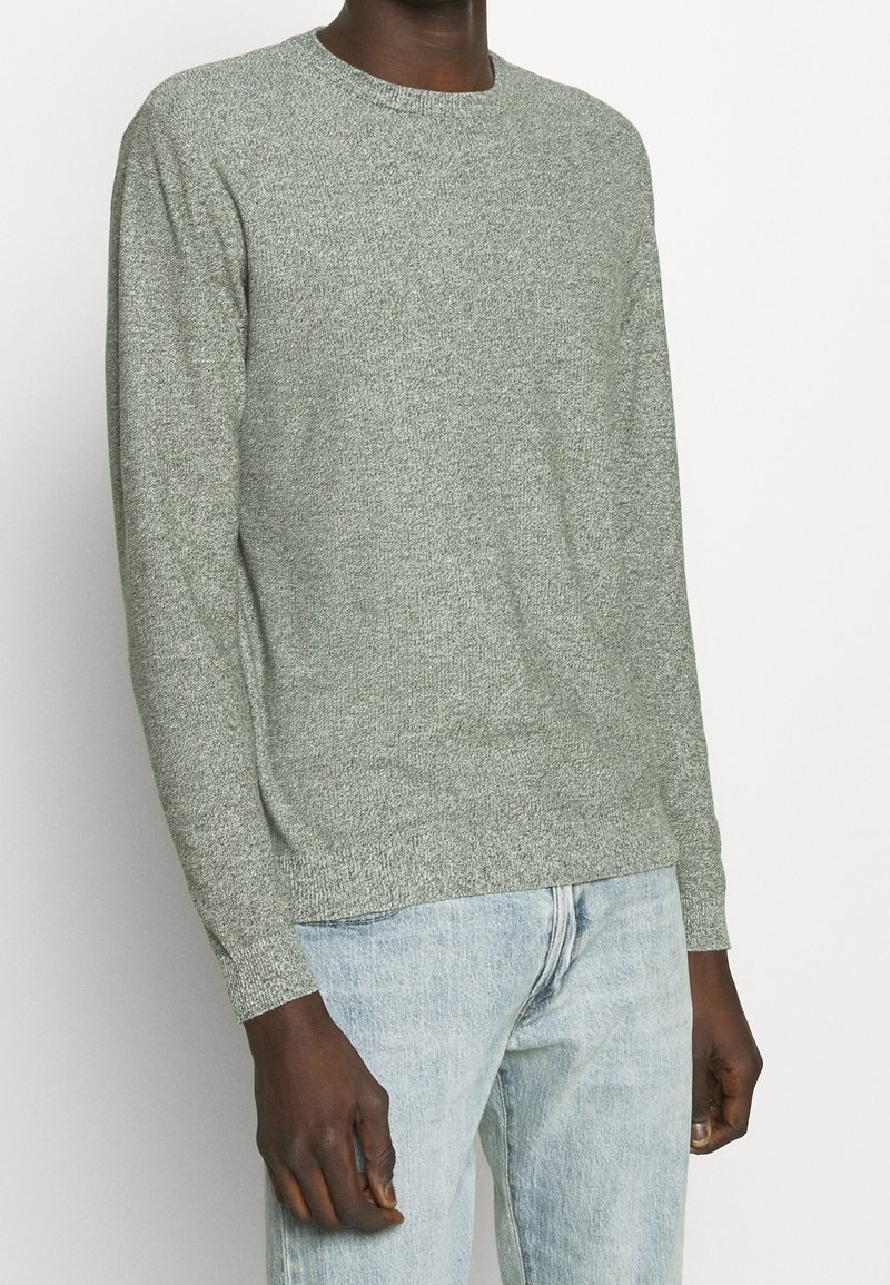 Jersey de punto gris con cuello redondo, puños acanalados y tejido texturizado, combinado con vaqueros azul claro.