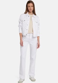 Giacca di denim bianca con accessori in argento, abbinata a un maglione a maglia color crema e jeans bianchi. Fit casual a gamba dritta e tessuto leggero.