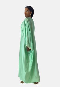 Abaya en satin vert menthe avec des manches longues, dotée d'accents décoratifs aux poignets et d'un design fluide, jusqu'au sol.