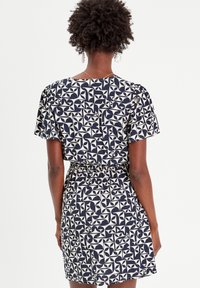 Robe à manches courtes avec un motif géométrique bleu marine et crème, taille cintrée et coupe décontractée, fabriquée dans un matériau léger.