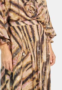 Vestido transparente con estampado floral, cuello con volantes, mangas largas y cintura atada. Presenta rayas doradas, marrones y rosas, con acentos de cuentas.