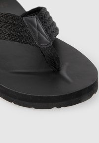 Svarta flip-flops med en texturerad vävd rem och en slät gummiaktig fotbädd med en lätt svängning. Designade med en tjock sula för stöd.