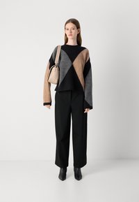 Sweater com um padrão em blocos de cor em bege, cinza e preto, com um corte relaxado e ombros caídos. Combinado com calças pretas ajustadas e botas de salto.