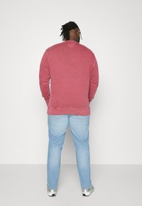 Sweatshirt roșu din bumbac cu guler rotund, având o textură fină și manșete ribbate, asortat cu blugi din denim de un albastru deschis.