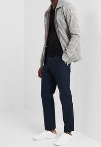 Veste à carreaux grise avec fermeture éclair sur le devant, t-shirt noir, pantalon bleu marine et baskets blanches. Tissu lisse avec des couleurs et motifs contrastés.