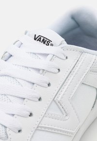 Sneaker bianco Vans con tessuto testurizzato e dettagli in pelle. Presenta stringhe piatte, un collare imbottito e un logo sulla linguetta.