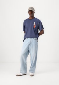 Navy blue cotton t-shirt with graphic print, light blue wide-leg jeans, gray cap, and white sneakers with brown accents. Simple, casual outfit.