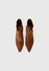 Botines de ante marrón hasta el tobillo con punta afilada y cierre lateral. Presenta una textura suave y un diseño minimalista.