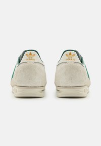 Adidas tenisky s krémovým semišovým materiálom, zelenými akcentmi a zlatým logom na päte. Okrúhly dizajn s textúrovanou zadnou časťou a svetlou podrážkou.