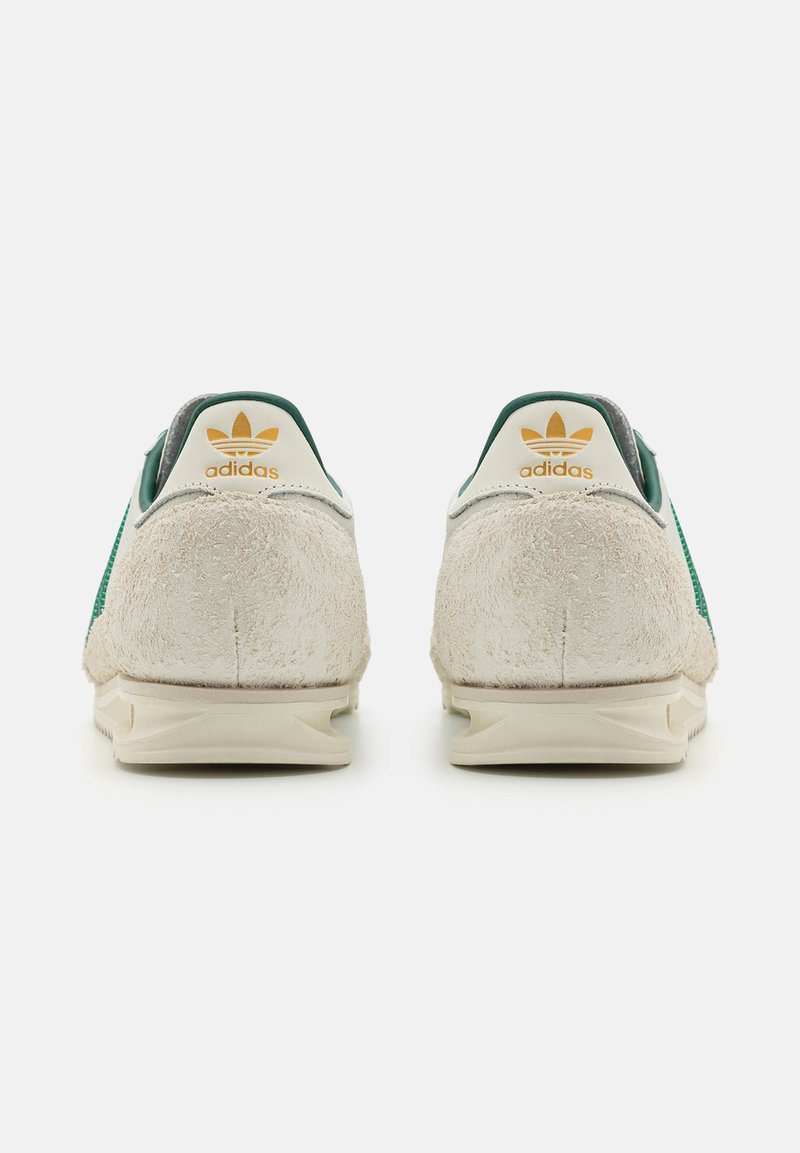 Baskets Adidas en suède crème, avec des accents verts et un logo doré au talon. Design arrondi avec un dos texturé et une semelle légère.