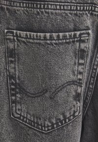 Szürke farmer hátul zsebe dupla varrással és finom hímzett hullámmintával a közepén.