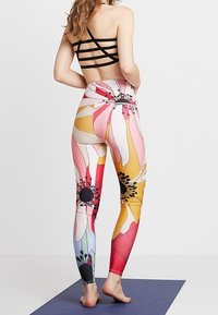 Leggings floraux multicolores avec une taille haute, ornés de grands motifs de fleurs roses et jaunes, et un soutien-gorge de sport noir à lanières.
