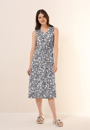 Sleeveless, v-neck dress with a black and white pattern, cinched waist, knee-length, and lightweight fabric. Paired with metallic sandals.