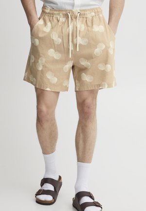 Beige shorts made of lightweight fabric, featuring a shell pattern in off-white. Elastic waistband with drawstring, two side pockets.