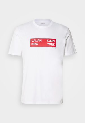 Bijela pamučna majica s kratkim rukavima koja sadrži podebljani crveni pravokutni grafički natpis: "CALVIN NEW KLEIN YORK." Ima dizajn s okruglim izrezom.