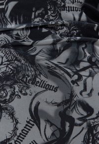 Tessuto elastico con una stampa nera e grigia caratterizzata da design astratti e dalla parola "ribelle". Texture liscia con un aspetto simile alla rete.