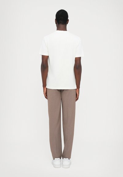 Hvid bomulds t-shirt med korte ærmer, parret med beige skræddersyede bukser og hvide sneakers; set fra ryggen.
