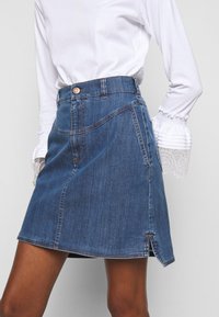 Jeanskjol med åtsittande midja, A-linjeform, blå färg, kontrasterande sömmar och sidofickor. Knäppning i midjan.