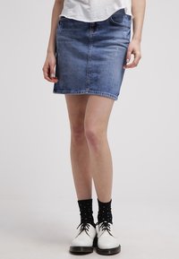 Jeansminikjol i medelblåtvätt, med en åtsittande silhuett, framfickor och en ren fåll, i kombination med vita skor och prickiga strumpor.